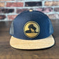 Wrath and Grace Logo Flatbill Snapback in Navy and Cork with Gold Patch